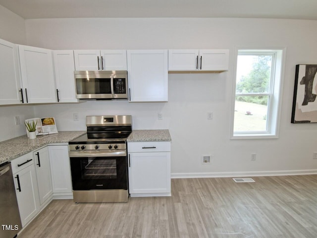 kitchen with light wood-type flooring, light stone counters, white cabinets, visible vents, and appliances with stainless steel finishes