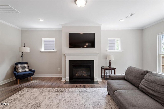living area featuring visible vents, a fireplace with flush hearth, wood finished floors, baseboards, and ornamental molding