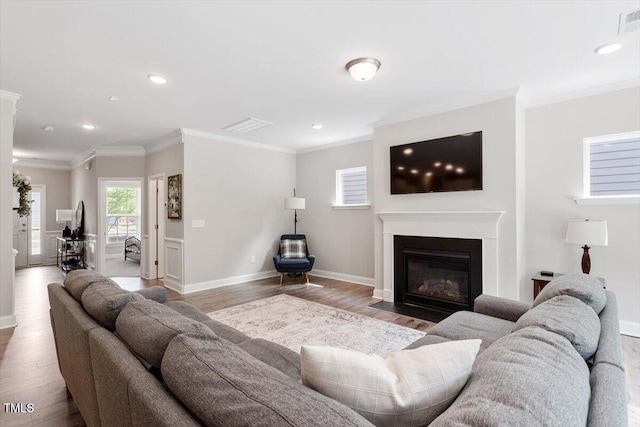 living room with recessed lighting, a fireplace with flush hearth, ornamental molding, and wood finished floors
