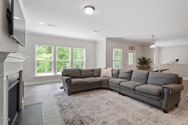 living room with visible vents, crown molding, wood finished floors, baseboards, and a fireplace with flush hearth