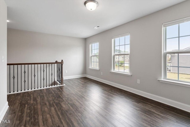 empty room featuring baseboards, dark wood-style floors, and visible vents