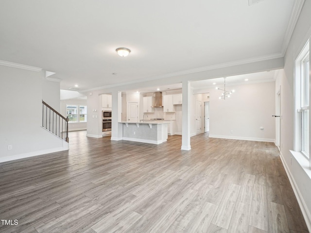 unfurnished living room featuring stairs, a sink, a notable chandelier, and light wood-type flooring