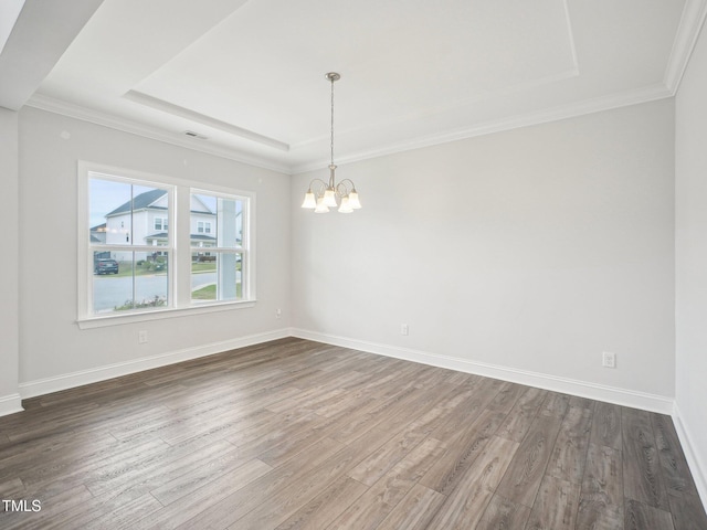 empty room featuring a chandelier, wood finished floors, baseboards, and a tray ceiling