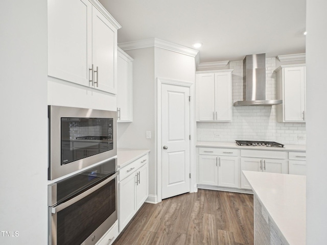 kitchen featuring wall chimney exhaust hood, stainless steel appliances, wood finished floors, light countertops, and ornamental molding