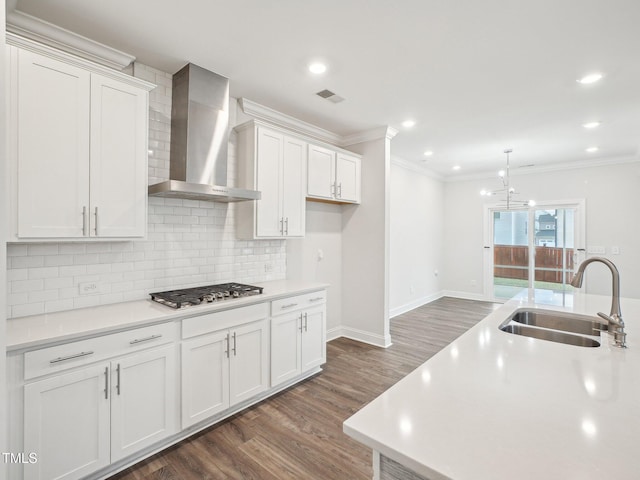 kitchen featuring visible vents, wall chimney range hood, a sink, dark wood-type flooring, and stainless steel gas cooktop