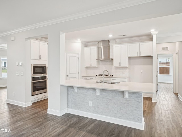 kitchen featuring wall chimney exhaust hood, stainless steel appliances, visible vents, white cabinetry, and wood finished floors