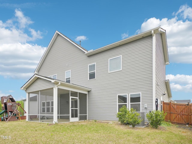rear view of property with a playground, a lawn, central air condition unit, fence, and a sunroom