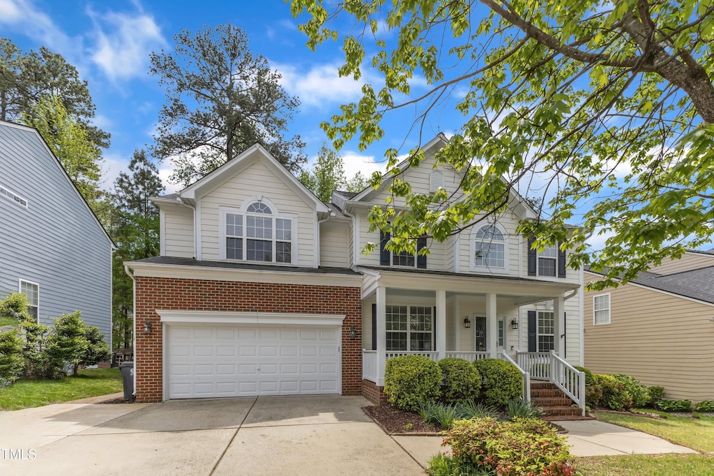 traditional home with concrete driveway, brick siding, an attached garage, and covered porch