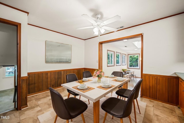 dining area with wainscoting, wood walls, plenty of natural light, a ceiling fan, and crown molding
