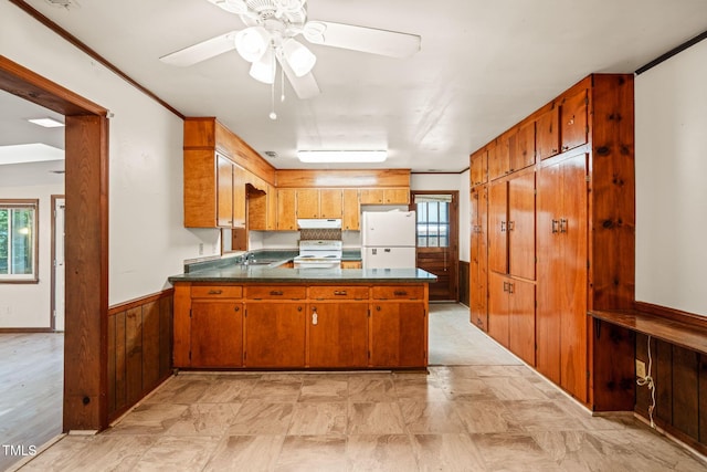 kitchen featuring white appliances, a sink, dark countertops, under cabinet range hood, and a peninsula