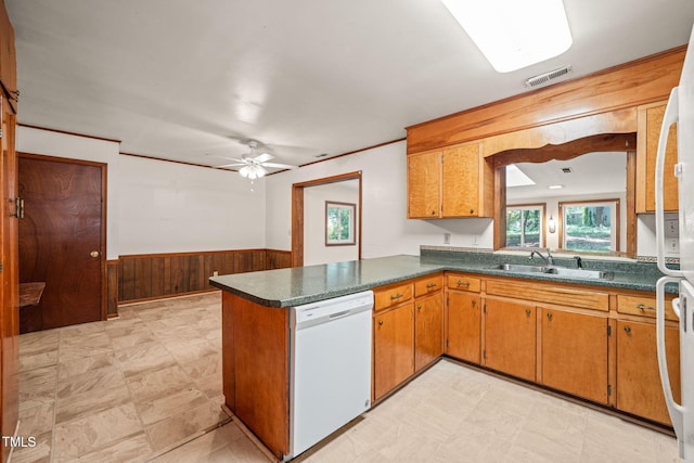 kitchen with dishwasher, dark countertops, a sink, wooden walls, and wainscoting