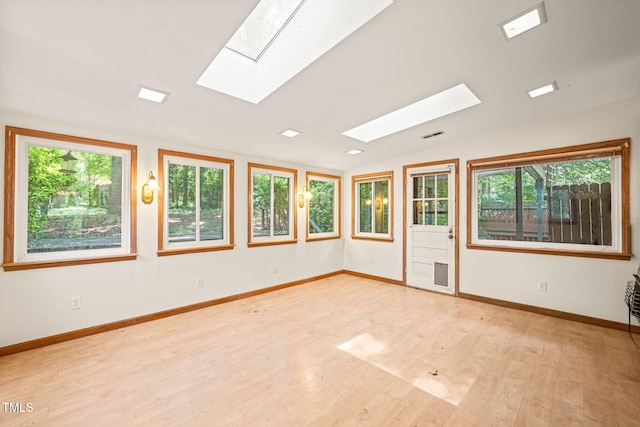 spare room featuring a skylight, light wood-style flooring, baseboards, and vaulted ceiling