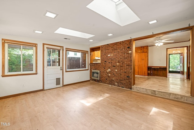 empty room with a skylight, heating unit, wood finished floors, and baseboards