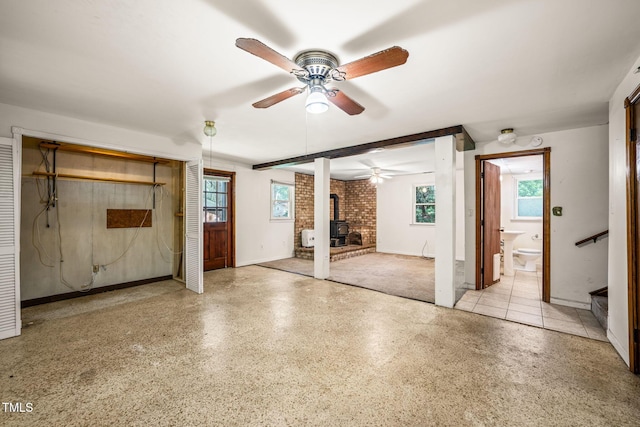 unfurnished living room with a wood stove, a ceiling fan, speckled floor, baseboards, and stairway