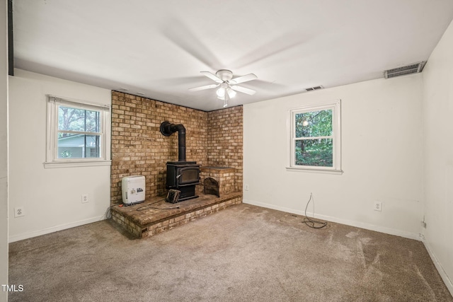 unfurnished living room featuring a wood stove, a ceiling fan, carpet flooring, and baseboards