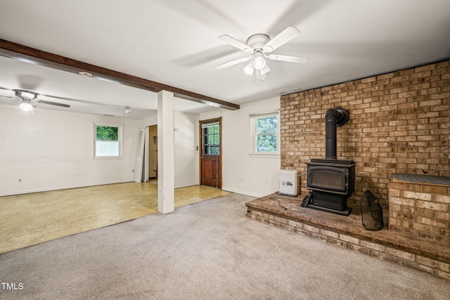 unfurnished living room with a ceiling fan, a wood stove, carpet flooring, baseboards, and beamed ceiling