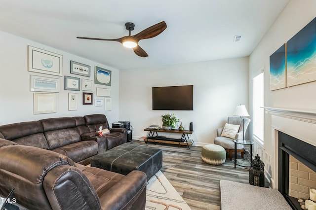living room with a ceiling fan, a fireplace with flush hearth, wood finished floors, baseboards, and visible vents