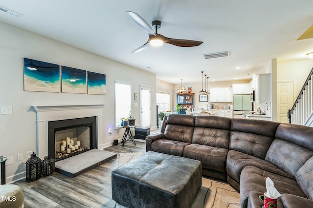 living area with light wood finished floors, visible vents, stairway, and a ceiling fan