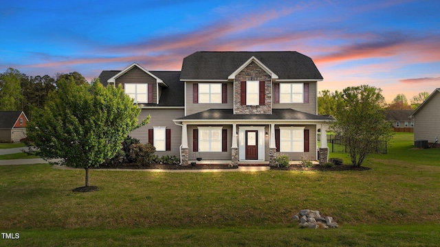 traditional-style house with a front yard, a porch, stone siding, and central AC unit