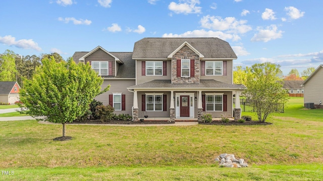 view of front facade with central AC, a porch, stone siding, a front lawn, and a shingled roof
