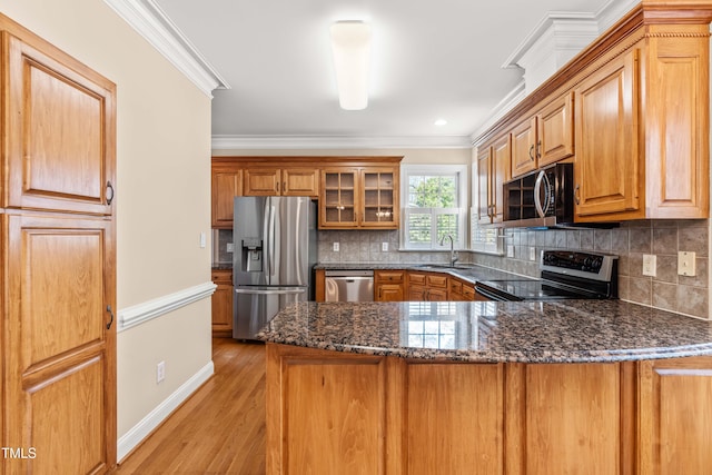 kitchen with brown cabinetry, ornamental molding, dark stone countertops, a sink, and stainless steel appliances