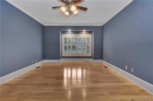 spare room featuring visible vents, light wood-style flooring, baseboards, ornamental molding, and a ceiling fan