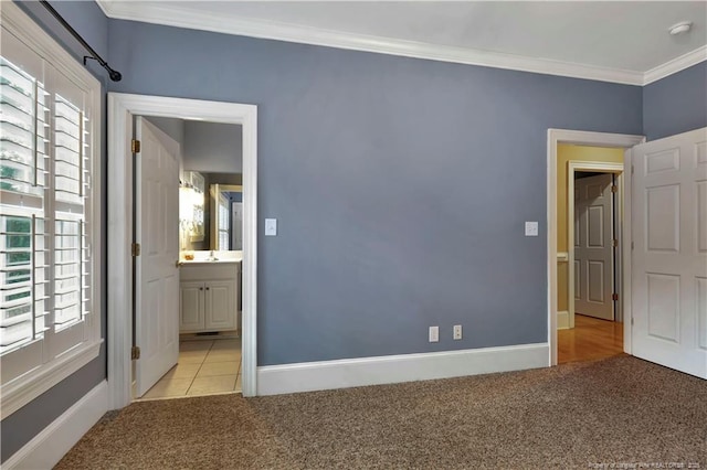 unfurnished bedroom with crown molding, baseboards, a sink, light carpet, and ensuite bathroom