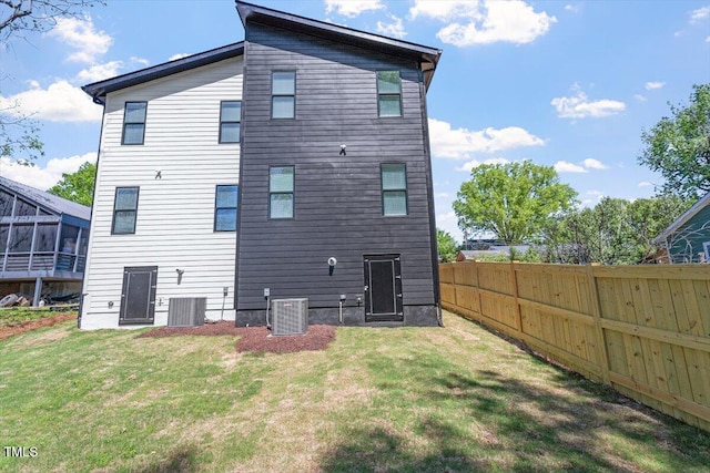 back of property with fence, central AC unit, and a lawn