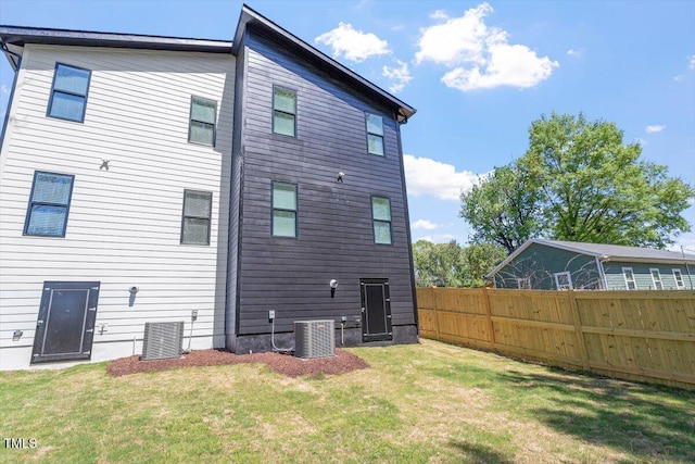 back of property with central air condition unit, fence, and a yard