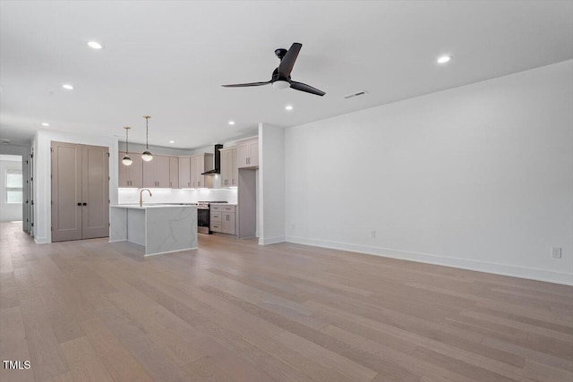 unfurnished living room with visible vents, a sink, ceiling fan, and light wood-type flooring