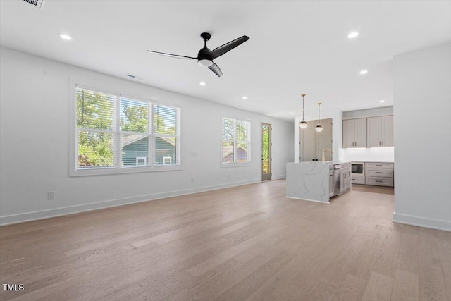 unfurnished living room featuring ceiling fan, a sink, baseboards, light wood-style floors, and recessed lighting