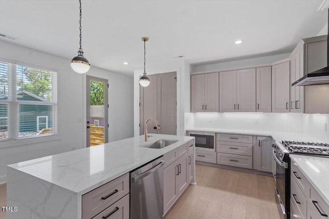 kitchen featuring visible vents, appliances with stainless steel finishes, a sink, light wood finished floors, and wall chimney exhaust hood