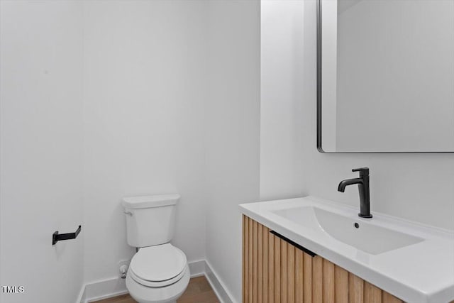 half bathroom with baseboards, vanity, and toilet
