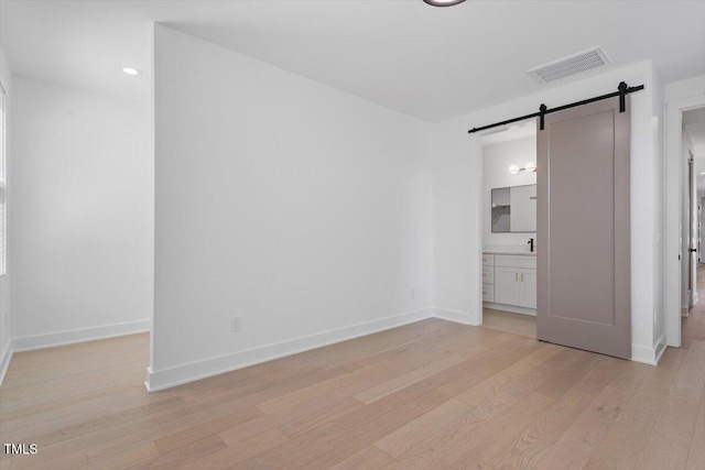 unfurnished bedroom with baseboards, visible vents, a barn door, and light wood-style flooring
