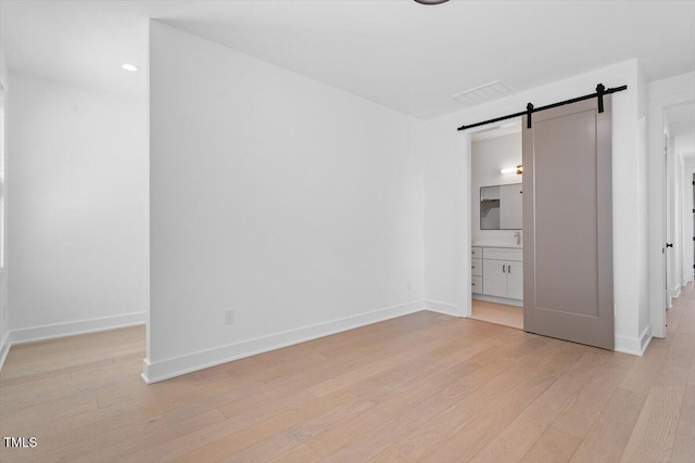 unfurnished bedroom featuring baseboards, light wood-style flooring, a barn door, and a walk in closet