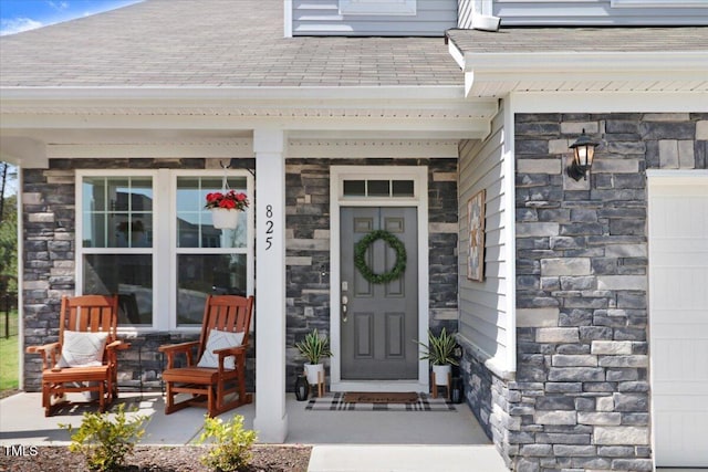 entrance to property with stone siding, covered porch, and roof with shingles