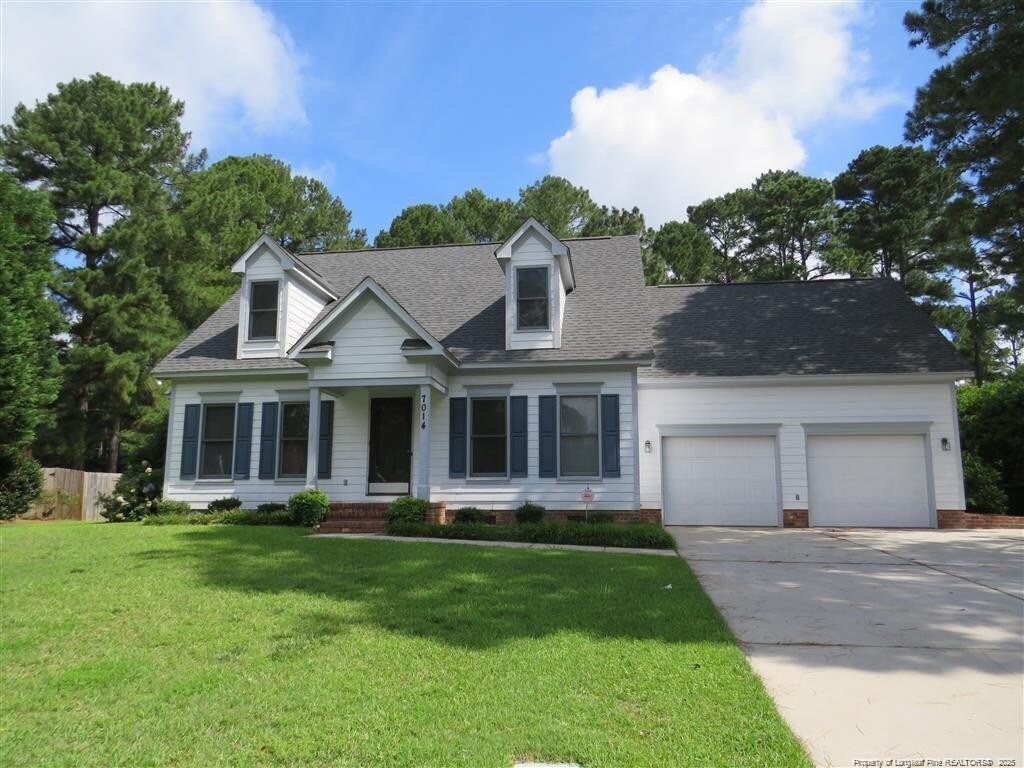 7014 Surrey Rd, Fayetteville, NC 28306 - cape cod home featuring driveway, a front yard, fence, an attached garage, and a shingled roof