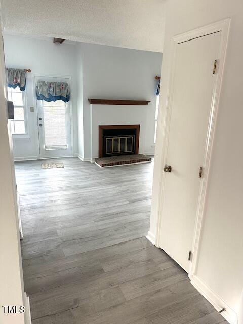 unfurnished living room featuring baseboards, a textured ceiling, wood finished floors, and a glass covered fireplace
