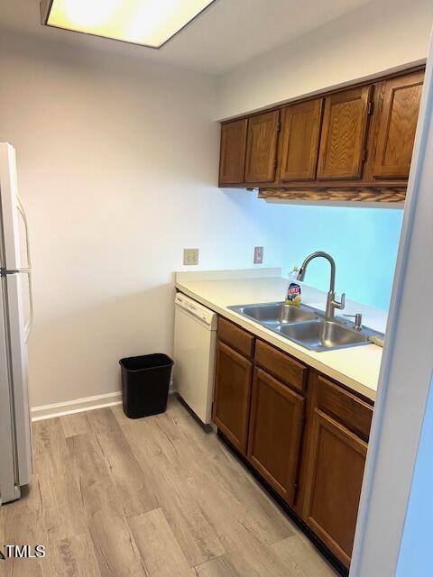 kitchen with light countertops, light wood finished floors, baseboards, white appliances, and a sink