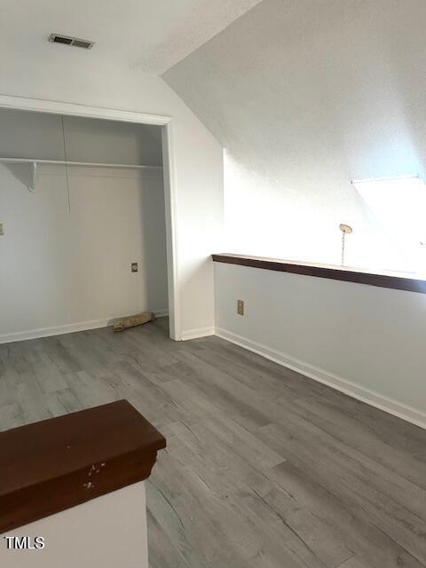 unfurnished bedroom featuring visible vents, a closet, wood finished floors, and vaulted ceiling