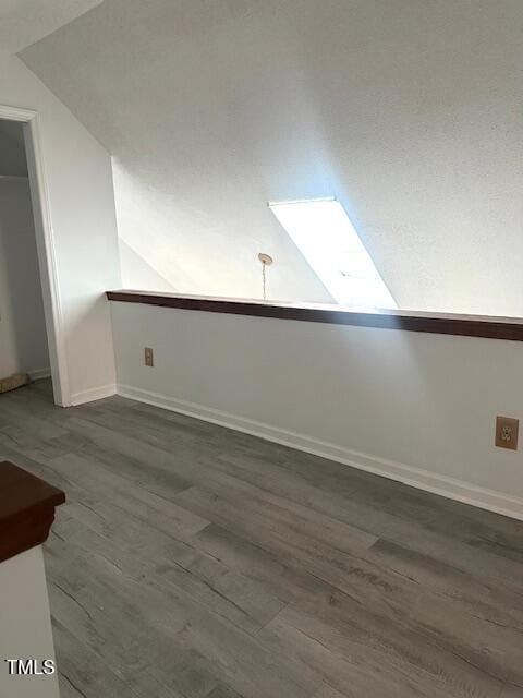 unfurnished room with dark wood-style flooring, baseboards, and vaulted ceiling with skylight
