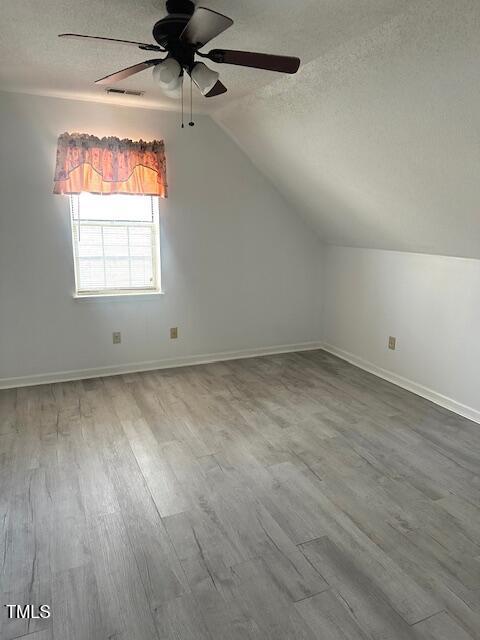 additional living space featuring visible vents, a ceiling fan, wood finished floors, and a textured ceiling