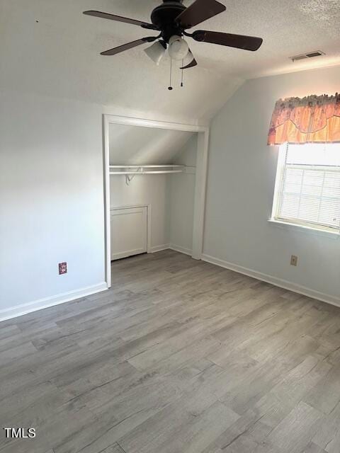 unfurnished bedroom with vaulted ceiling, a closet, wood finished floors, a textured ceiling, and visible vents