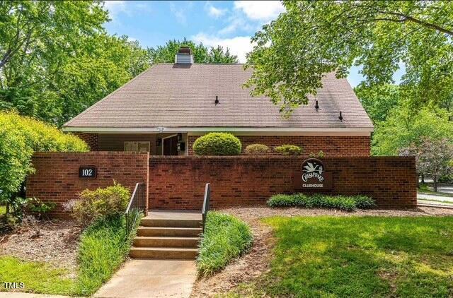 rear view of house featuring a chimney, roof with shingles, brick siding, and a yard