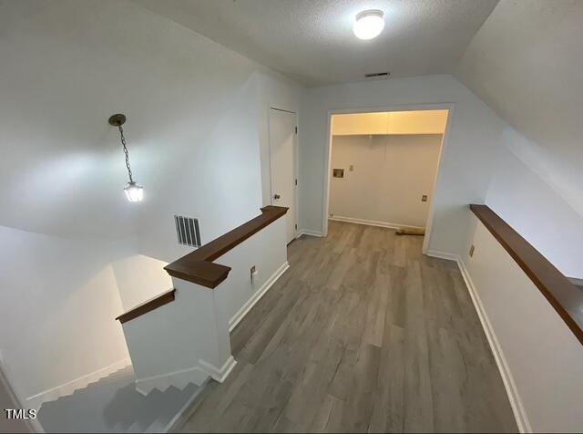 hall featuring visible vents, wood finished floors, an upstairs landing, and a textured ceiling