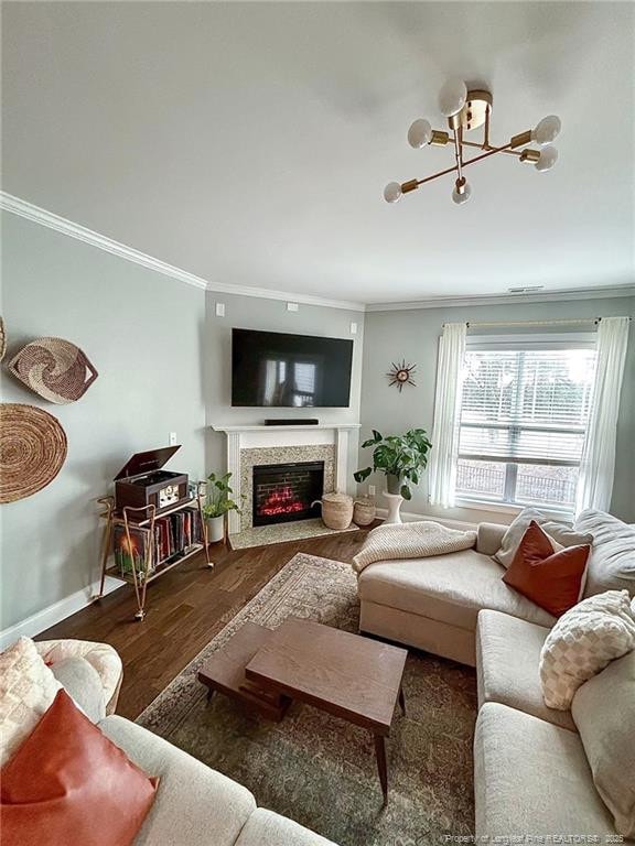 living room with a premium fireplace, ornamental molding, baseboards, a chandelier, and wood finished floors