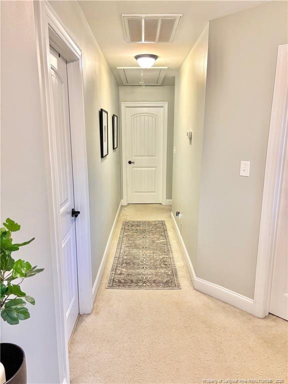 corridor with baseboards, visible vents, attic access, and light colored carpet