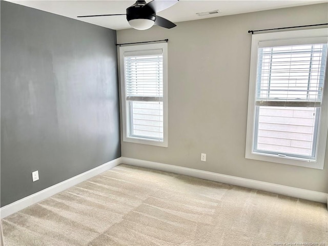 carpeted spare room with a wealth of natural light, visible vents, baseboards, and a ceiling fan