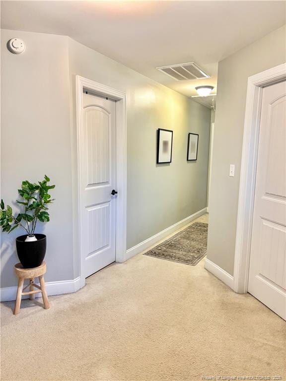 corridor with baseboards, visible vents, and light colored carpet
