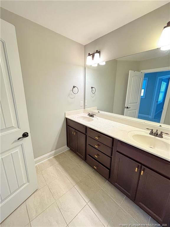 full bathroom with double vanity, baseboards, a sink, and tile patterned flooring